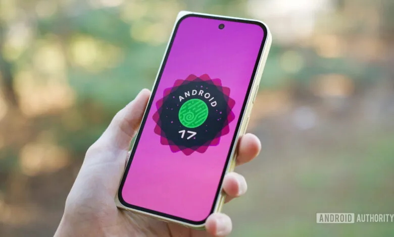 Hand holding smartphone displaying Android 17 logo on pink screen.
