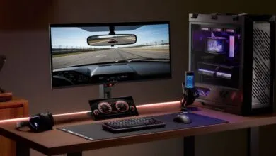 Gaming setup with monitor displaying race car view, PC, keyboard, mouse, and accessories.