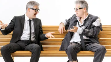 Businessman in suit talks to his homeless, tattered self on bench.