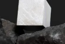 Concrete cube resting on dark, textured basalt rocks against black backdrop.