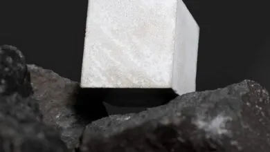 Concrete cube resting on dark, textured basalt rocks against black backdrop.