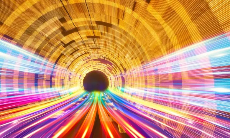 Abstract tunnel with bright, blurred lines of light in yellow, pink, blue, and purple.