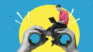 Person sits on binoculars using laptop, against yellow and blue background.