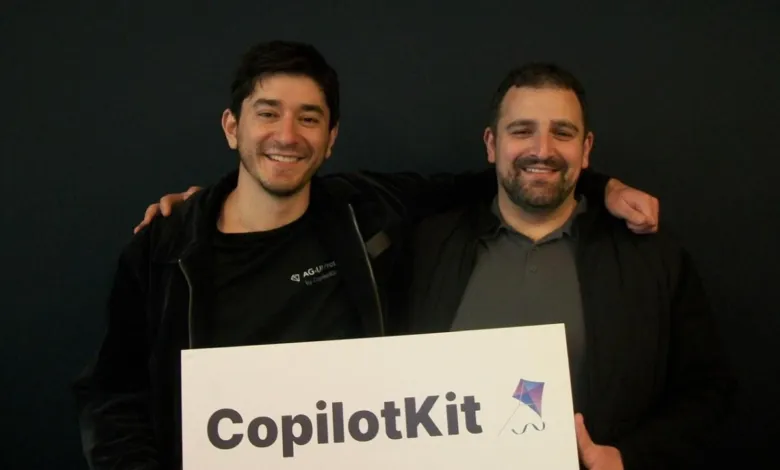 Two smiling men holding a CopilotKit sign in front of a dark background.