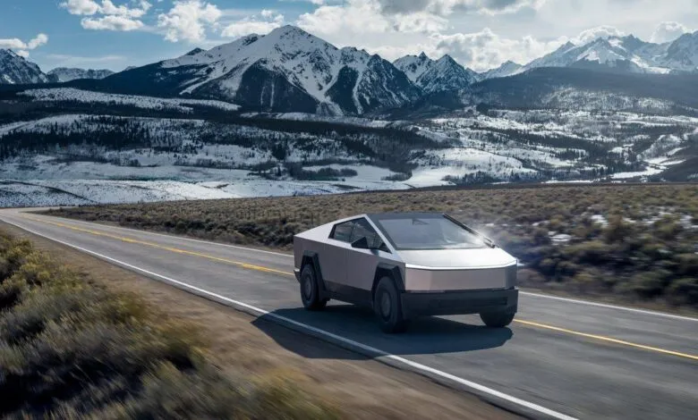 Tesla Cybertruck driving on a road with snow-capped mountains in the background.