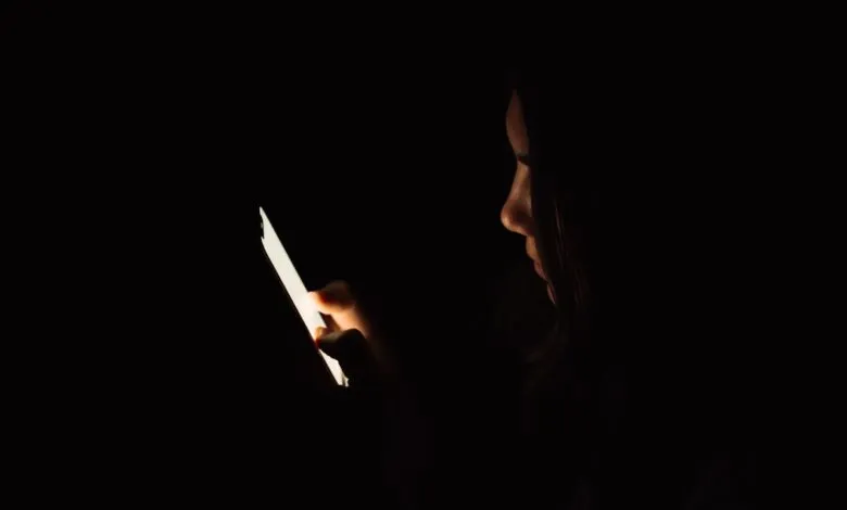 Person in the dark illuminated by the light of a smartphone screen.