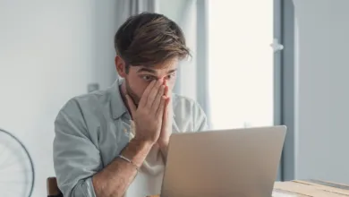 Man with hands on face looking at laptop, appearing stressed or shocked.