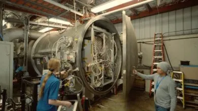 Two people working on a large, open, cylindrical machine with complex wiring and components.