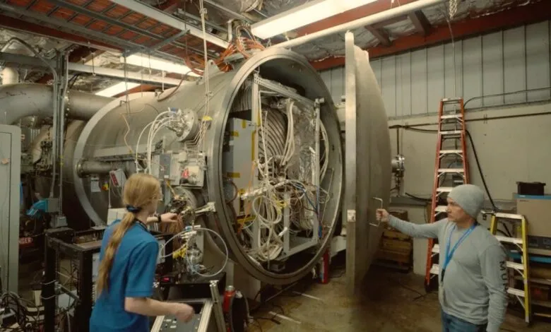 Two people working on a large, open, cylindrical machine with complex wiring and components.
