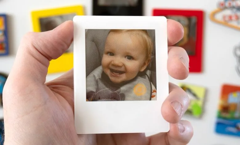 Hand holds a magnet with a smiling baby photo.