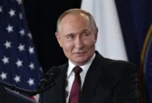 Vladimir Putin at podium with US flag backdrop.