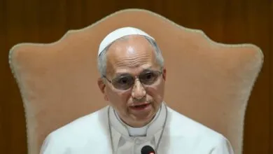 Archbishop Claudio Gugerotti speaking at a microphone, wearing glasses.