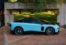 Light blue Ferrari with black roof parked on brick driveway near modern building.