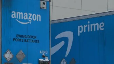 Two blue Amazon delivery trucks with the Amazon and Prime logos.