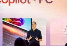 Man presents new Copilot+ PC on stage with laptop displays.