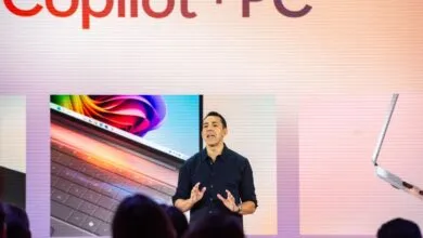 Man presents new Copilot+ PC on stage with laptop displays.