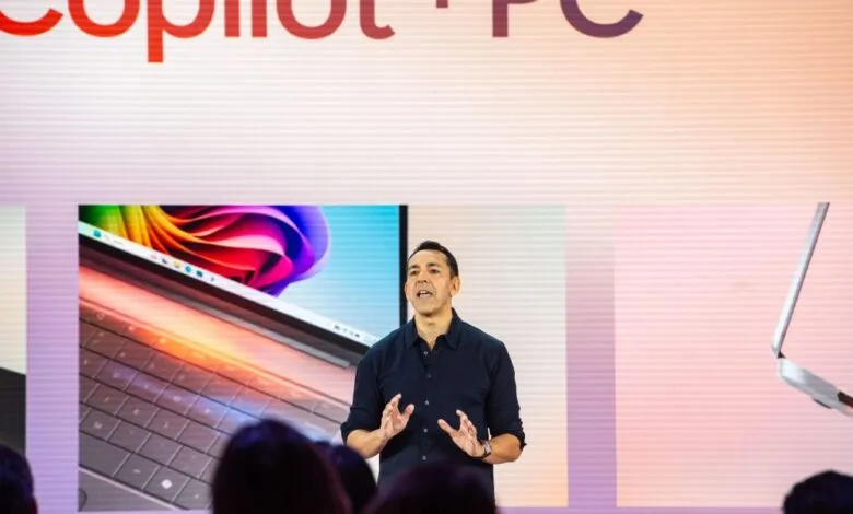 Man presents new Copilot+ PC on stage with laptop displays.