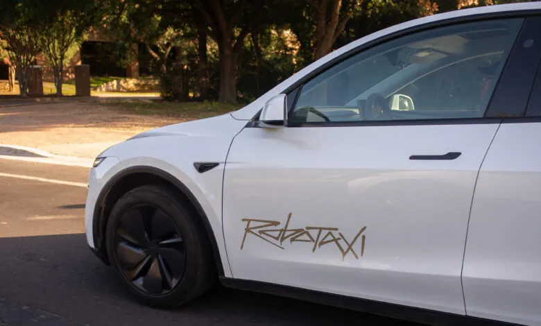 White Tesla car with 'Robotaxi' graphic on the side, driving on a road.