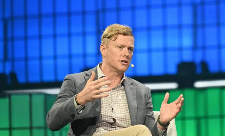 Man with blond hair gestures during a presentation.