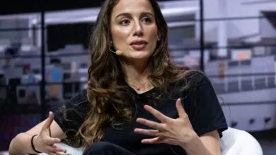 Woman with microphone gestures while speaking on stage.