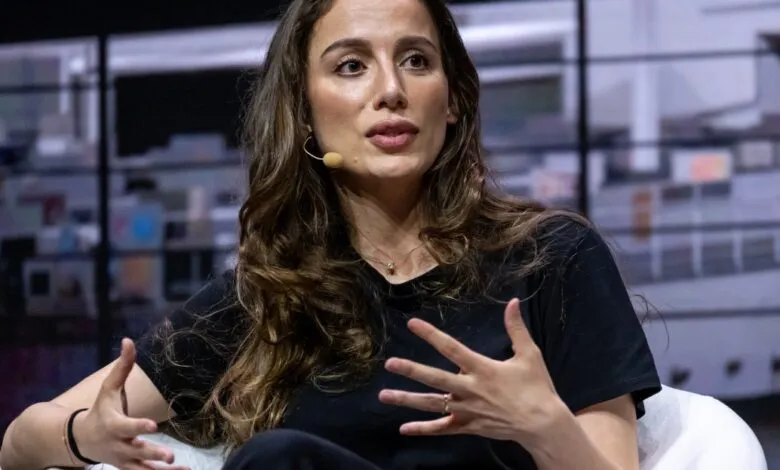 Woman with microphone gestures while speaking on stage.
