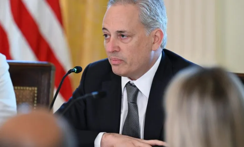 Man in suit at meeting with American flag in background.