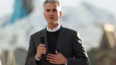 Man in suit speaks into microphone outdoors.