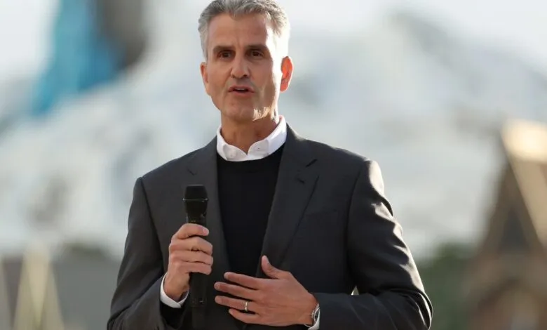 Man in suit speaks into microphone outdoors.