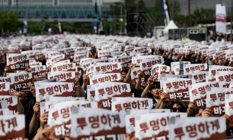 Large crowd holding signs with Korean text, demanding transparency.