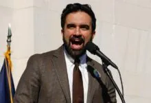 Man in suit speaks passionately at microphone, outdoors.