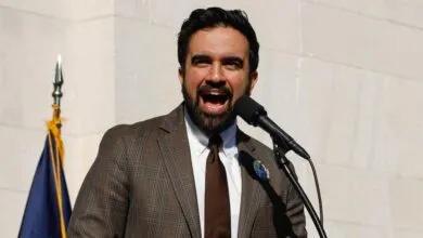 Man in suit speaks passionately at microphone, outdoors.