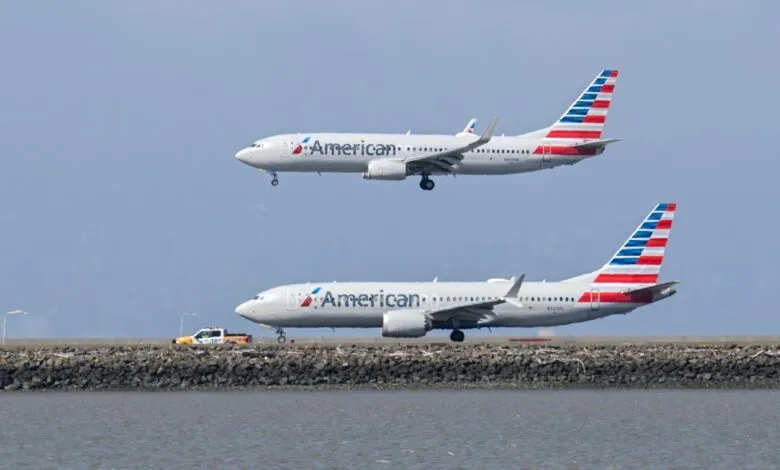 Two American Airlines planes, one landing, one on the ground, against a blue sky.
