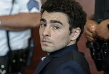 Man with curly hair looks over shoulder, surrounded by law enforcement.