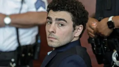 Man with curly hair looks over shoulder, surrounded by law enforcement.