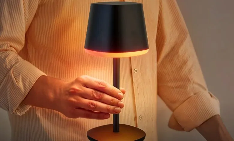 Person adjusting a modern black table lamp with a warm orange glow.