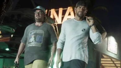 Two men stand in front of a building at night, one wearing a humorous t-shirt.