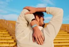 Man stretches arms behind back wearing fitness tracker outdoors.