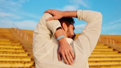 Man stretches arms behind back wearing fitness tracker outdoors.