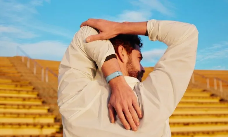 Man stretches arms behind back wearing fitness tracker outdoors.