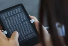 Hands holding a Kindle e-reader displaying text, focus on the screen.