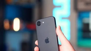 Hand holding a gray iPhone with Apple logo visible on the back.