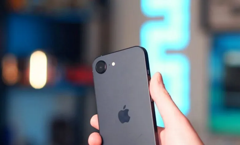 Hand holding a gray iPhone with Apple logo visible on the back.