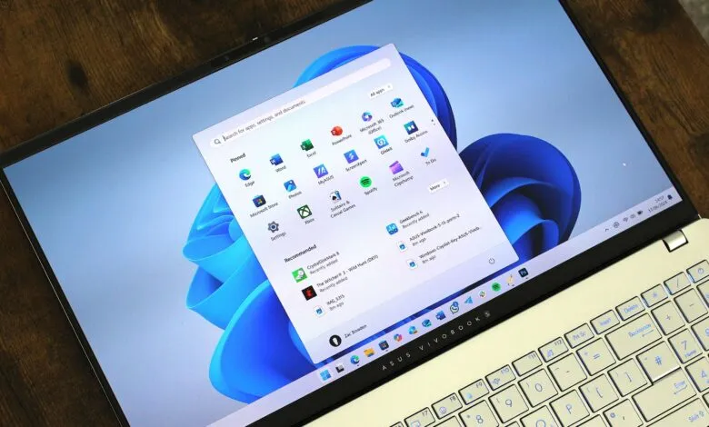 Asus Vivobook laptop displaying Windows 11 start menu on a wooden surface.
