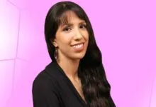 Portrait of a smiling woman with long dark hair against a pink background.