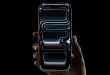 Hand holding a dark iPhone with a glowing abstract design on the screen.