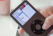Hand holding an iPod Classic showing the music menu.