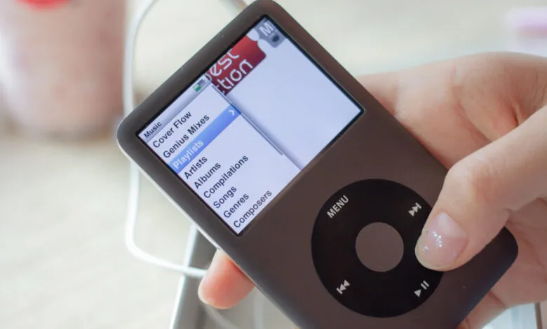 Hand holding an iPod Classic showing the music menu.