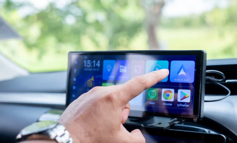 Hand touches Android Auto icon on car infotainment system.
