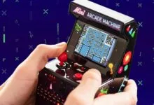 Hands play a mini arcade machine with pixelated game on a blue background.