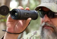 Man in camo hat uses a handheld thermal monocular for observation.